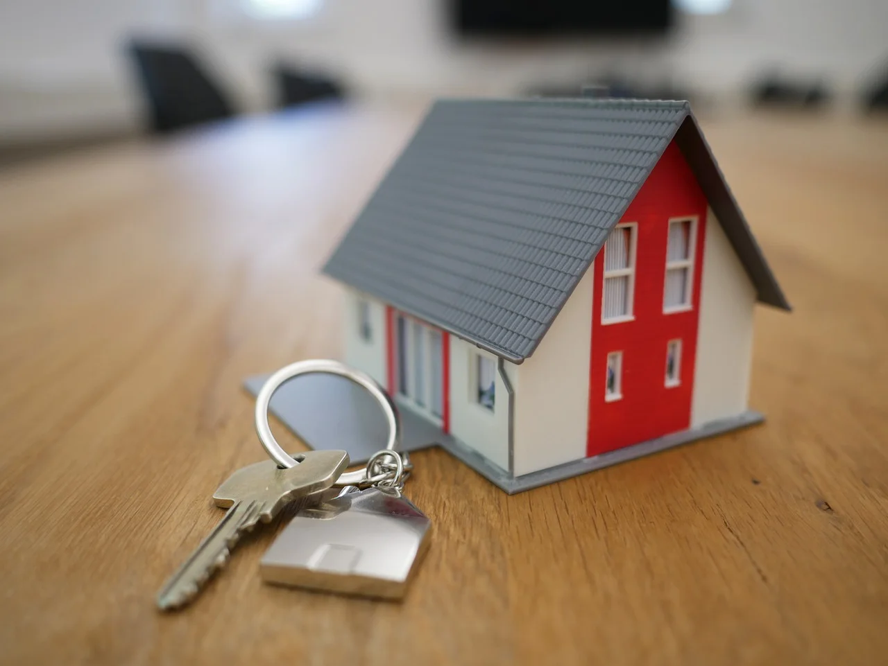 Maquette de maison au toit gris et clés posées sur une table en bois.